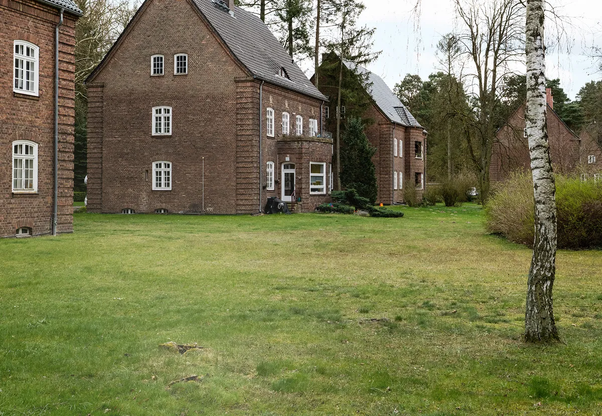 Hero Image Gartenansicht auf doppelstöckige rote Klinkerbauten umrahmt von
Bäumen.